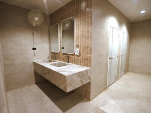 A modern bathroom with a large sink, two mirrors, a wall-mounted fan, and a door.