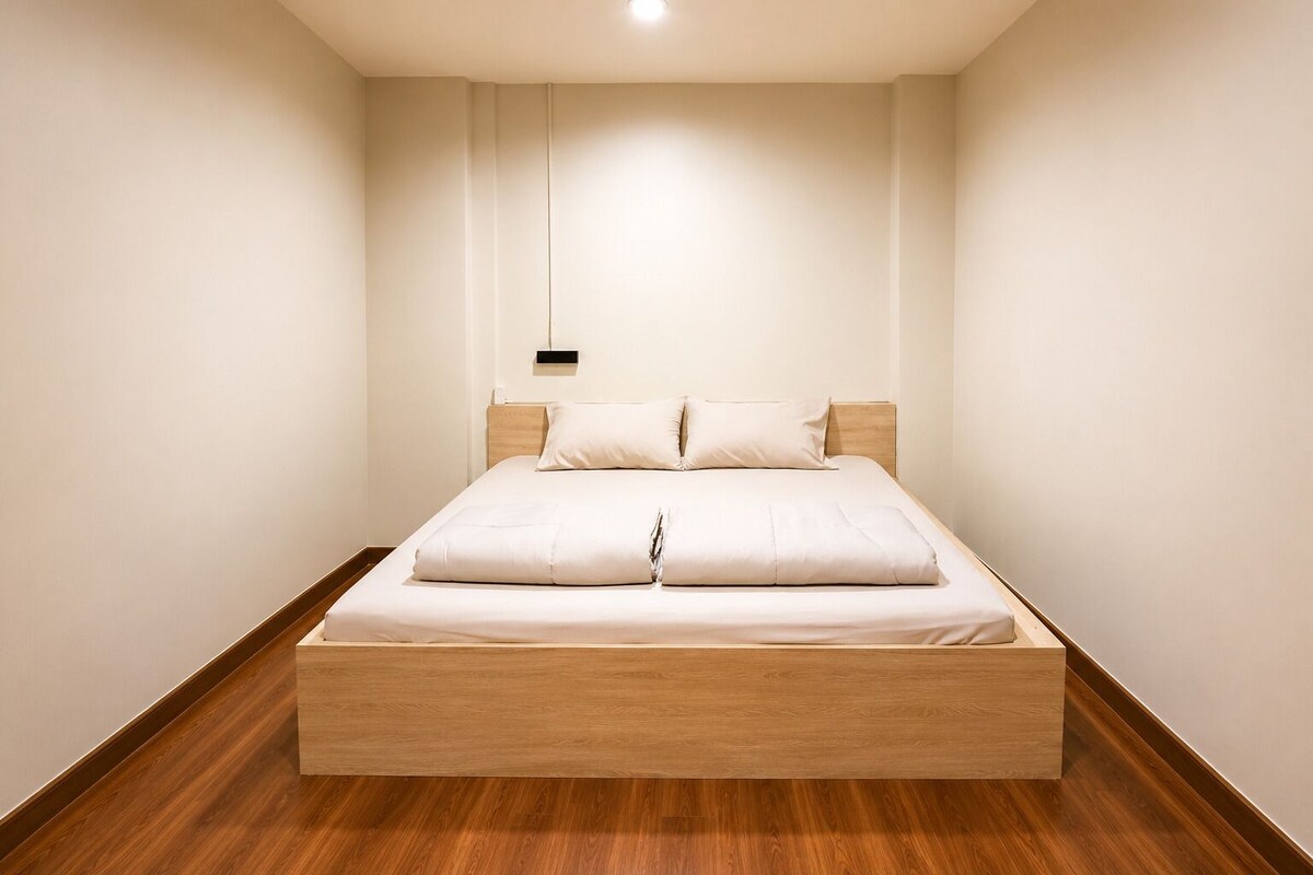 A minimalist bedroom with a wooden platform bed, white bedding, and a pendant light.