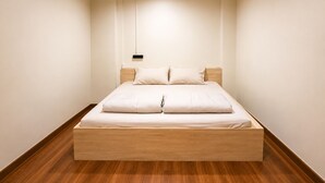 A minimalist bedroom with a wooden platform bed, white bedding, and a pendant light.