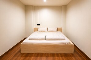 A minimalist bedroom with a wooden platform bed, white bedding, and a pendant light.