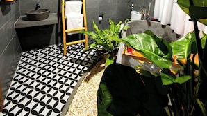 Une salle de bain moderne avec un sol à motifs noir et blanc, une échelle en bois, un miroir rond, un lavabo et une grande plante verte.