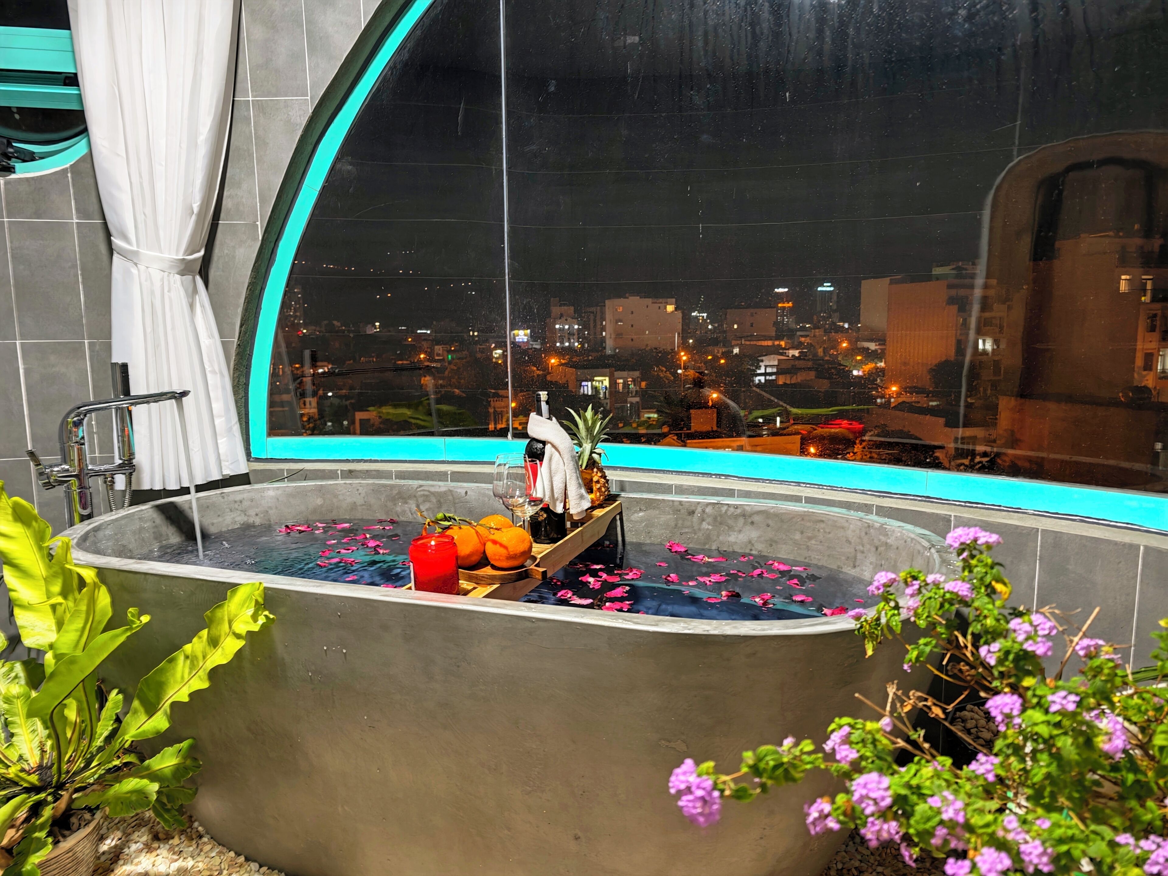 Una bañera con vistas a la ciudad, una toalla, una botella y algunas frutas.