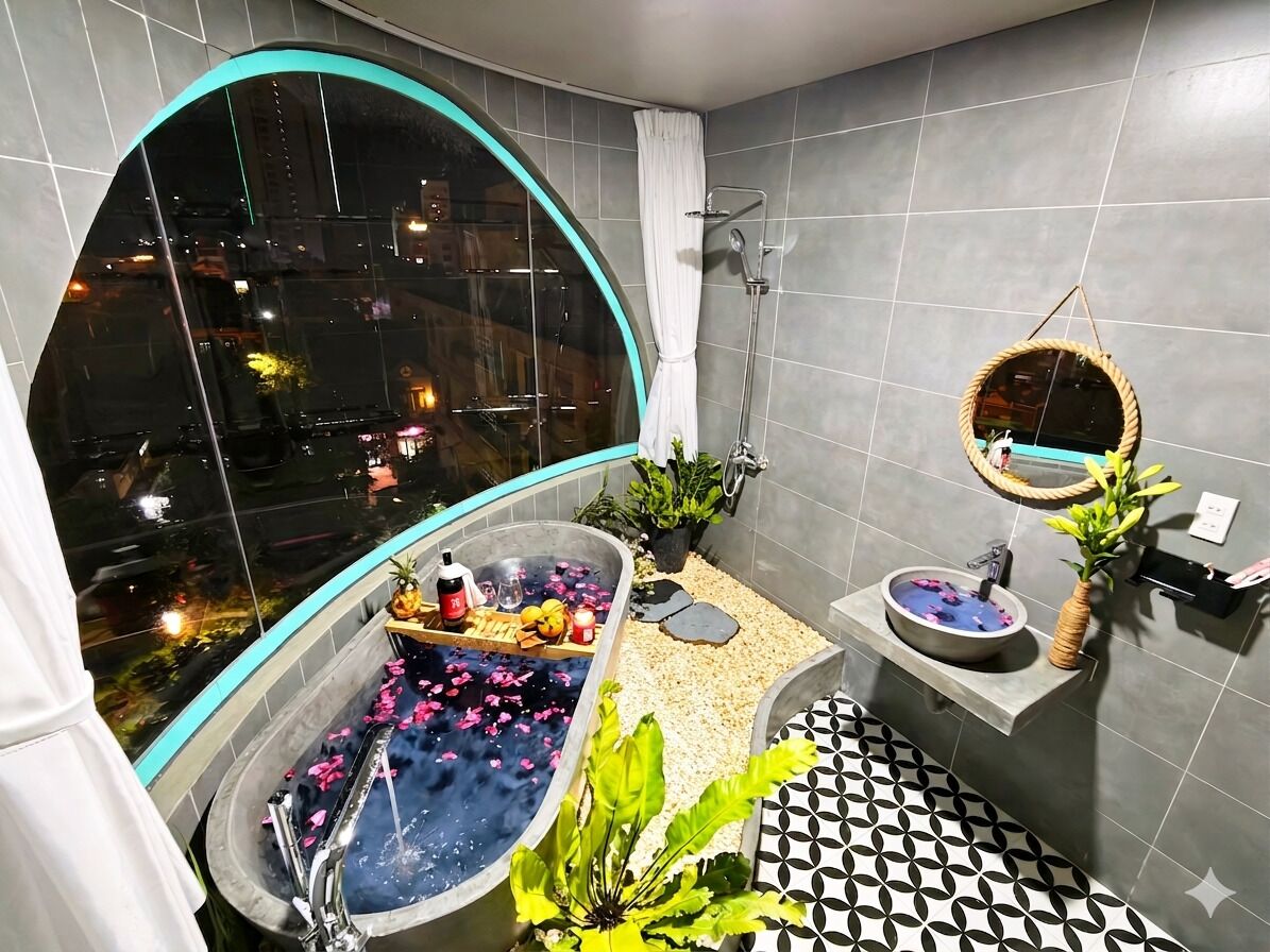 Un baño moderno con una bañera grande, ducha, felpudo de baño colgado y vista de la ciudad por la noche.