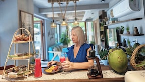 Un comedor con una mesa preparada para dos personas, que incluye una cesta de frutas, un vaso de bebida roja y un plato con comida.