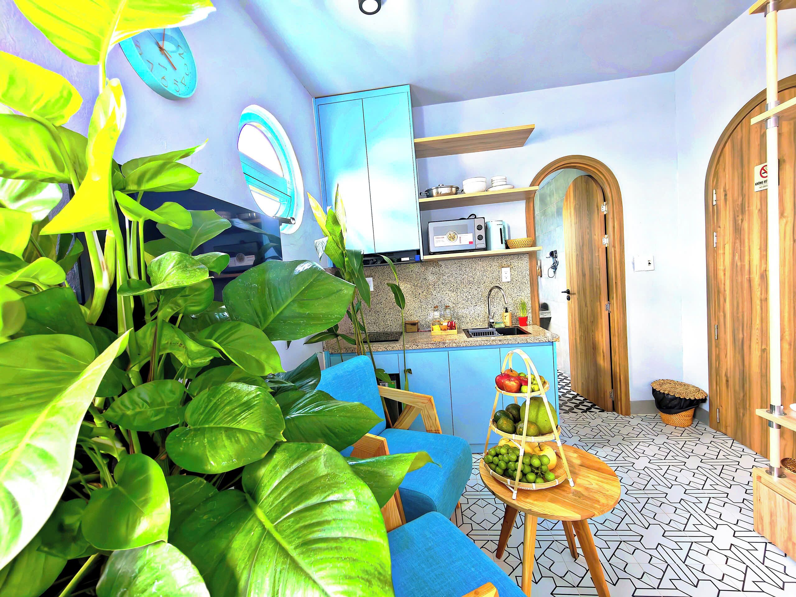 Una cocina compacta con un lavamanos, un microondas y un armario azul. Hay una cesta de frutas sobre una mesita y un sofá azul en la habitación.