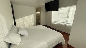 Ein Schlafzimmer mit einem Bett, einem an der Wand befestigten Fernseher und einem Fenster mit Jalousien.
