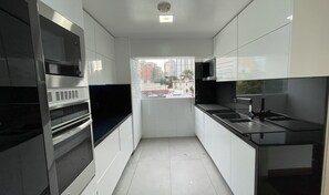 Een moderne keuken met roestvrijstalen apparatuur, witte kasten en uitzicht op de stad door een raam.