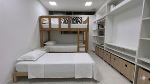 Een slaapkamer met stapelbed, een houten ladder, witte beddengoed en ingebouwde planken met boeken.