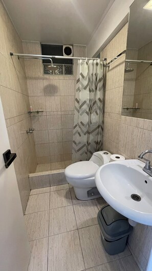 Een badkamer met een douche, toilet, wastafel en een prullenbak.