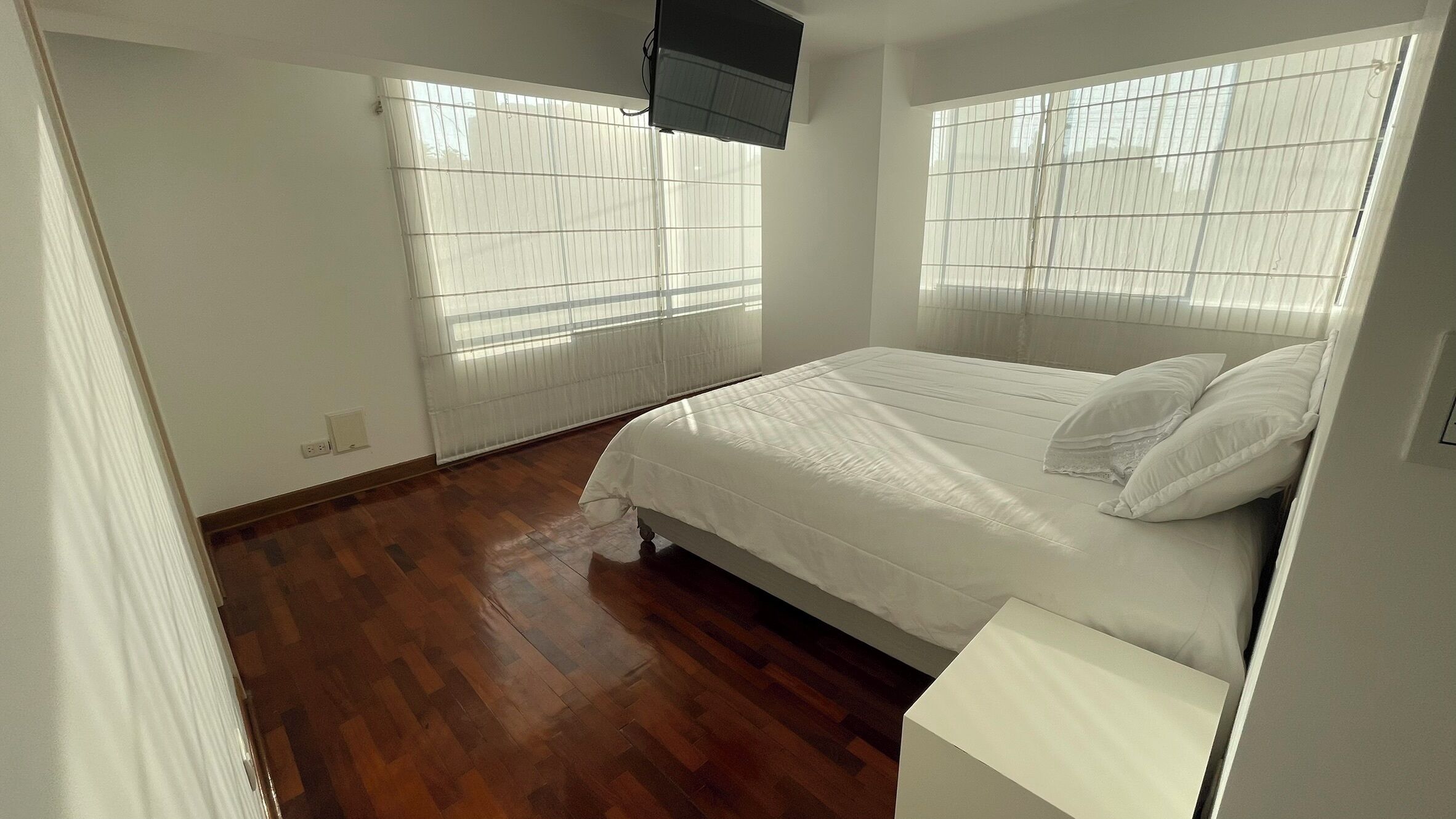 A bedroom with a bed, wooden flooring, and a window with blinds.