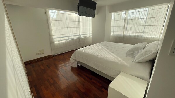 Een slaapkamer met een bed, houten vloeren en een raam met jaloezieën.