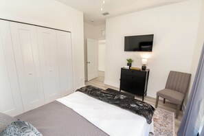 Een slaapkamer met een bed, een kledingkast, een televisie, een stoel en een kleine tafel met een plant.
