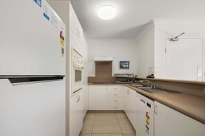 A compact kitchen with white cabinets, a microwave, a sink, and a stove. - Miami Beachside - 32 (Gold Coast)
