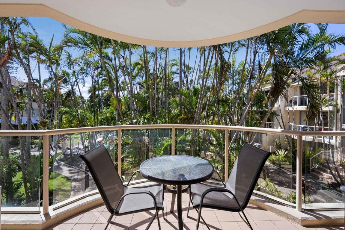 Un balcon avec une table ronde et deux chaises, donnant sur un paysage tropical avec des palmiers.