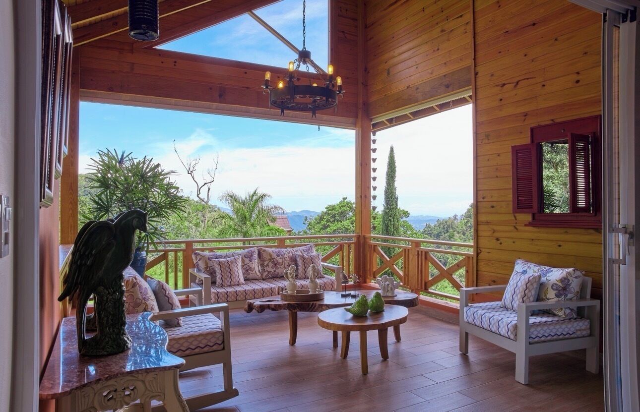 A wooden deck with a sofa, chairs, and a table, overlooking a scenic landscape.