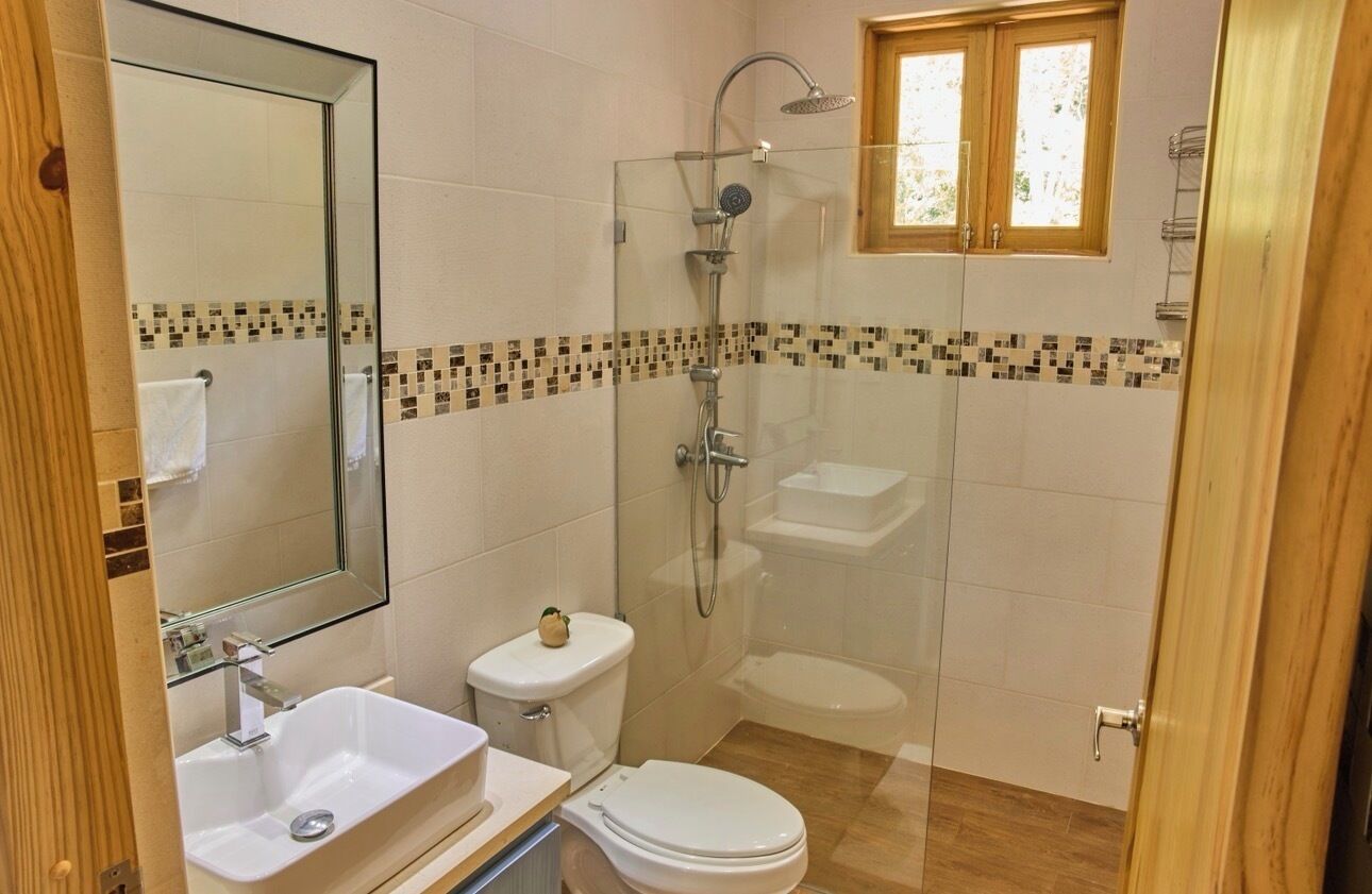 Casa de banho com cabine de duche envidraçada, sanita, lavatório e espelho.