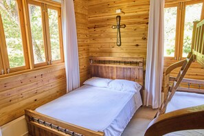 Una habitación de cabaña de madera con una cama, un cabecero de madera y una ventana con cortinas.