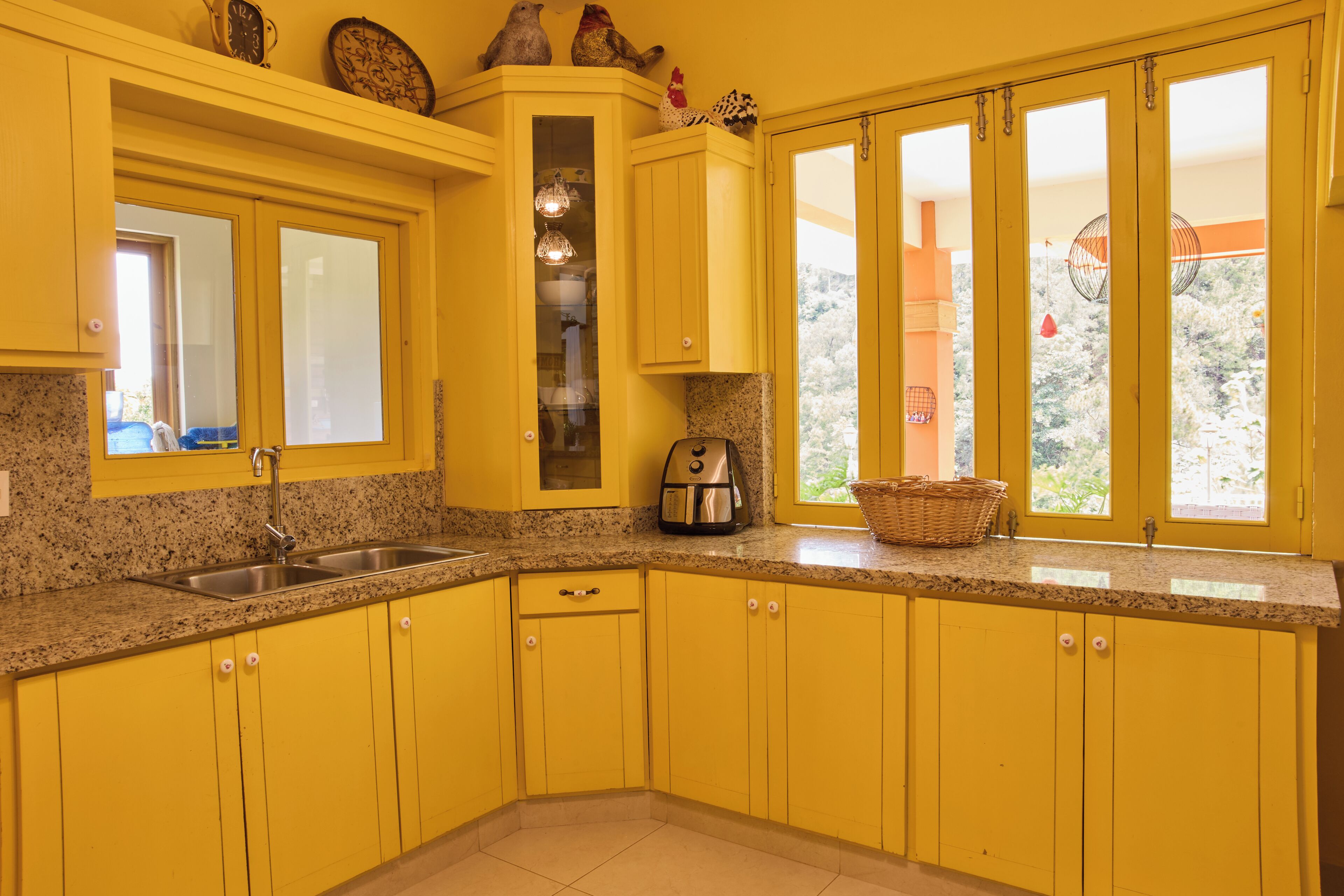 Una cocina con armarios amarillos, encimera de granito, cafetera y ventana con vista a árboles.