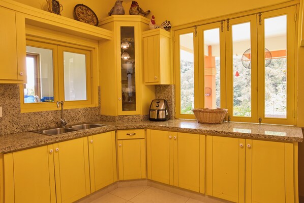A kitchen with yellow cabinets, a granite countertop, a coffee maker, and a window with a view of trees.
