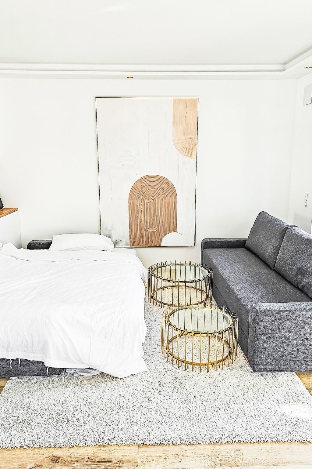 Ein Schlafzimmer mit einem Bett, einem grauen Sofa, einem weißen Teppich und einer Wand mit einem großen abstrakten Gemälde.