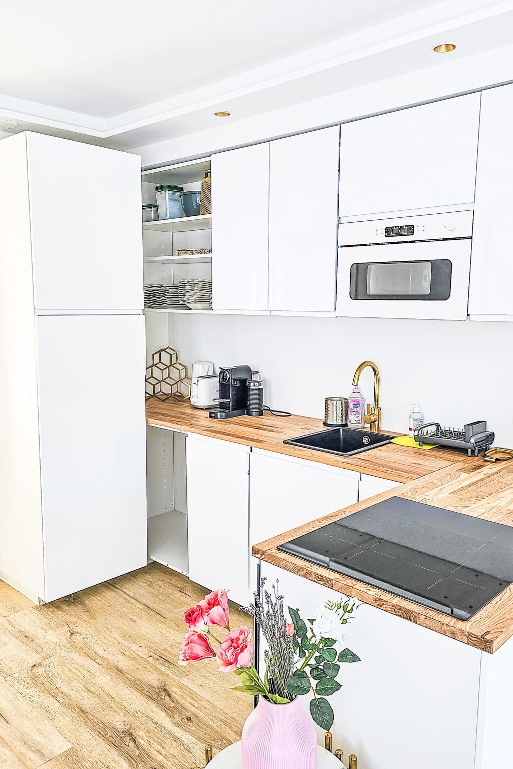 Eine moderne Küche mit weißen Schränken, einer Holzarbeitsplatte, einem eingebauten Backofen und einem Spülbecken.