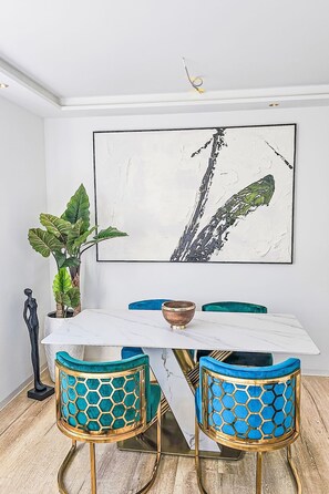 A dining area with a white marble table, two blue chairs with gold legs, a large abstract painting on the wall, and a potted plant. - Luxus Neubau by Interhome (Munich)