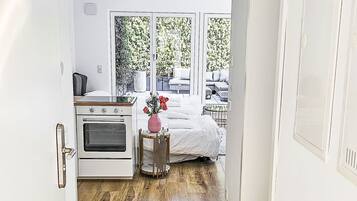 Ein Flur, der zu einem Schlafzimmer mit Bett, einem kleinen Tisch mit einer Vase und einer Küchenzeile mit Backofen führt.