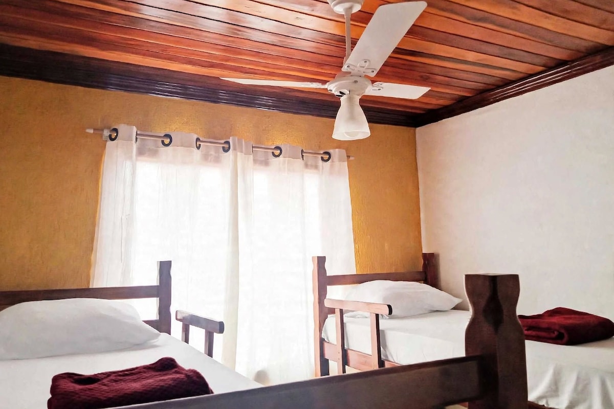 A room with two beds, a ceiling fan, and a window with curtains.
