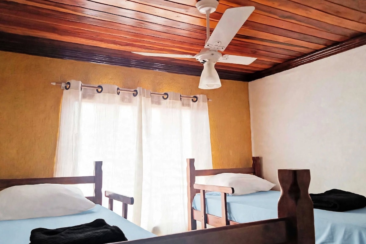 A room with two wooden beds, a ceiling fan, and a window with curtains.