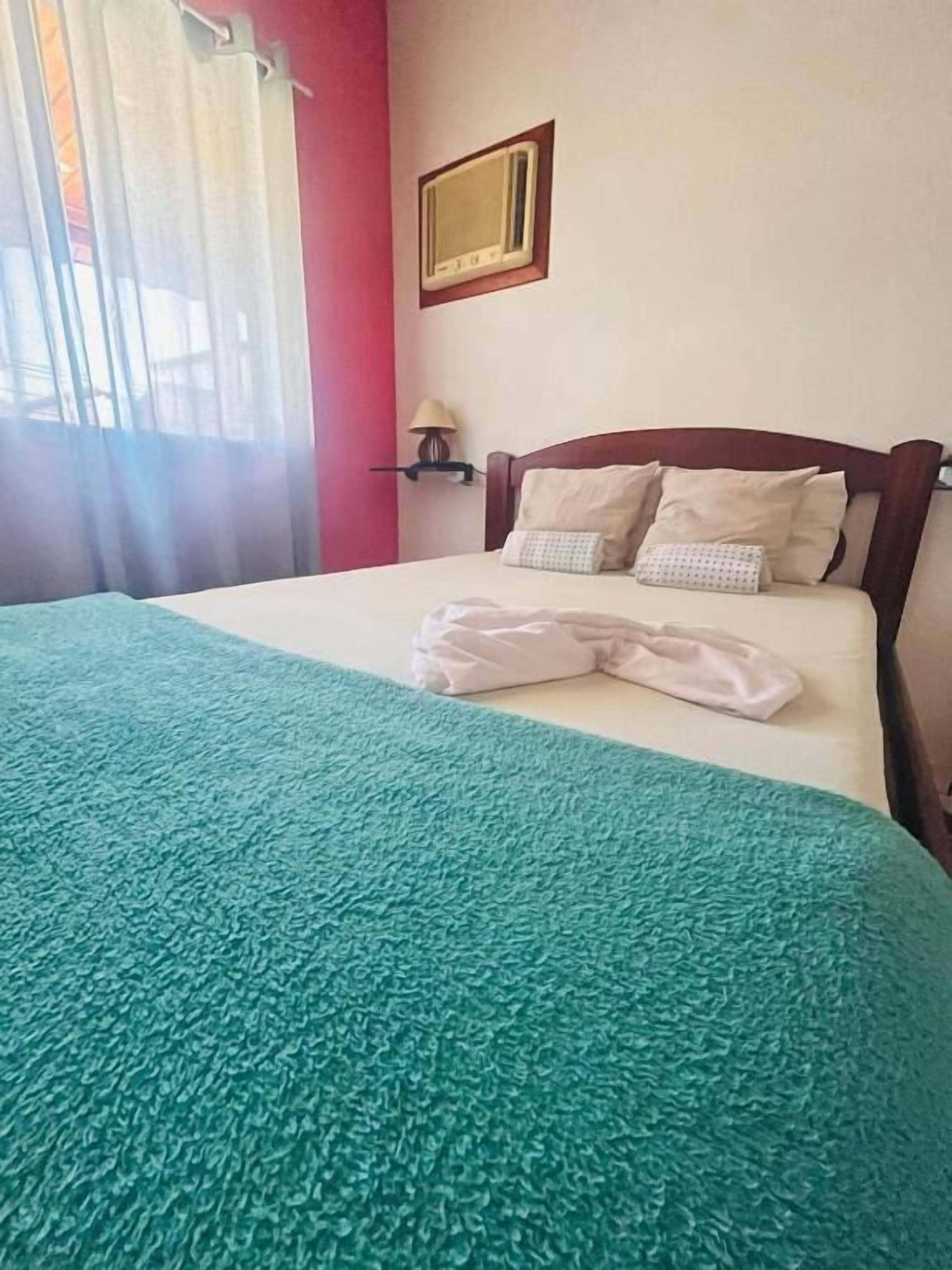 A bed with a teal blanket, a wooden headboard, and a wall-mounted lamp.