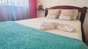 A bed with a teal blanket, a wooden headboard, and a wall-mounted lamp.
