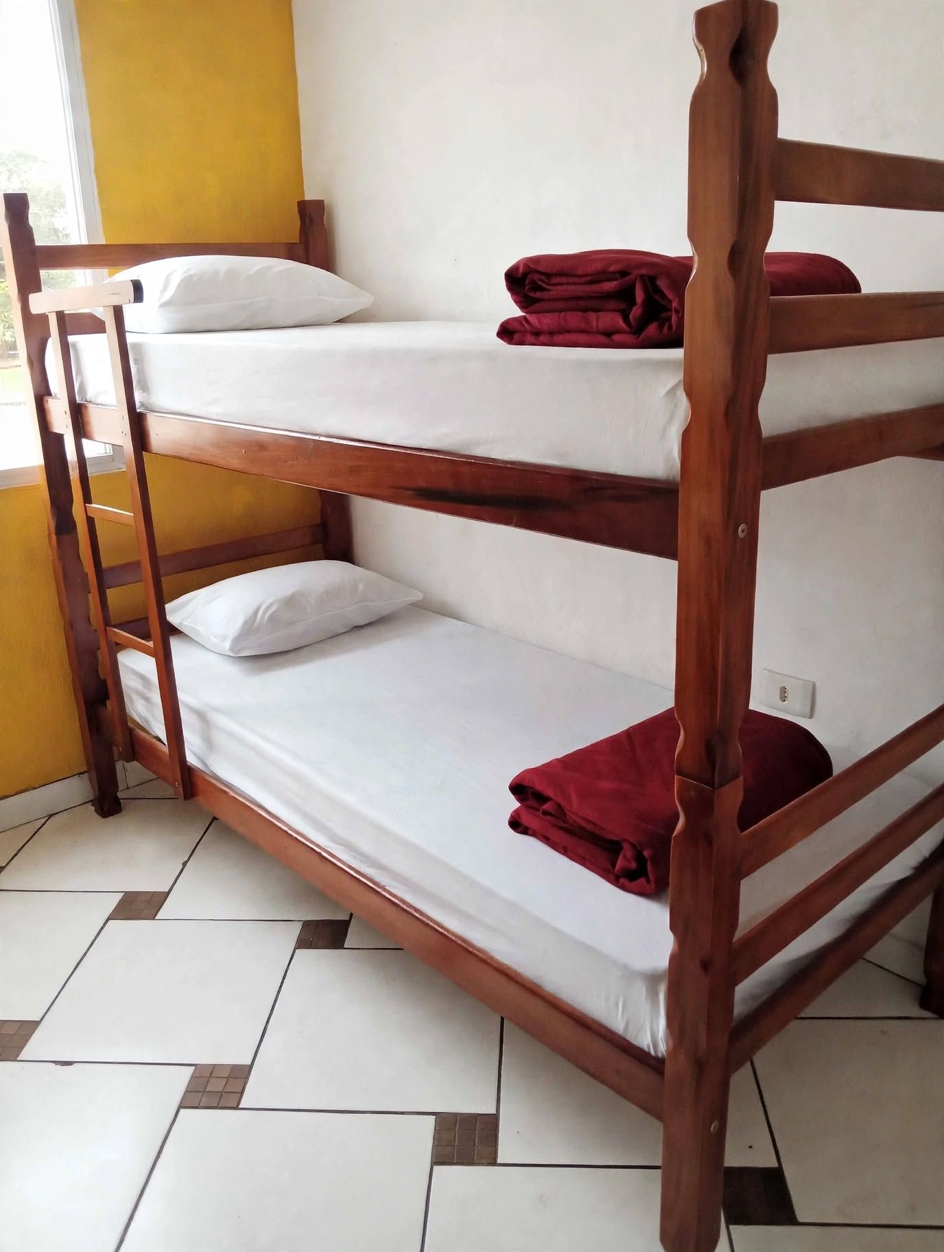 A bunk bed with a ladder, white bedding, and a red blanket.