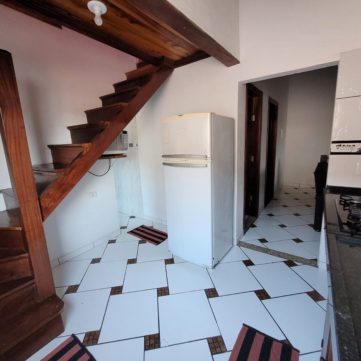 Eine Küche mit einem weißen Kühlschrank, einer Holztreppe und Fliesenboden.