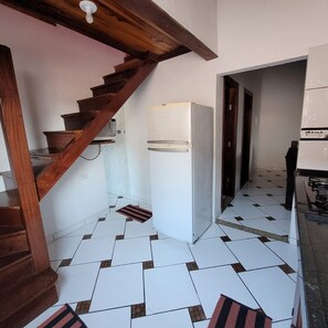Una cocina con refrigerador blanco, escalera de madera y suelo de baldosas.