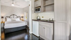 Ein Schlafzimmer mit Bett, Nachttischen und Deckenventilator. Angrenzend befindet sich eine Küchenzeile mit Mikrowelle, Spüle und Schränken.