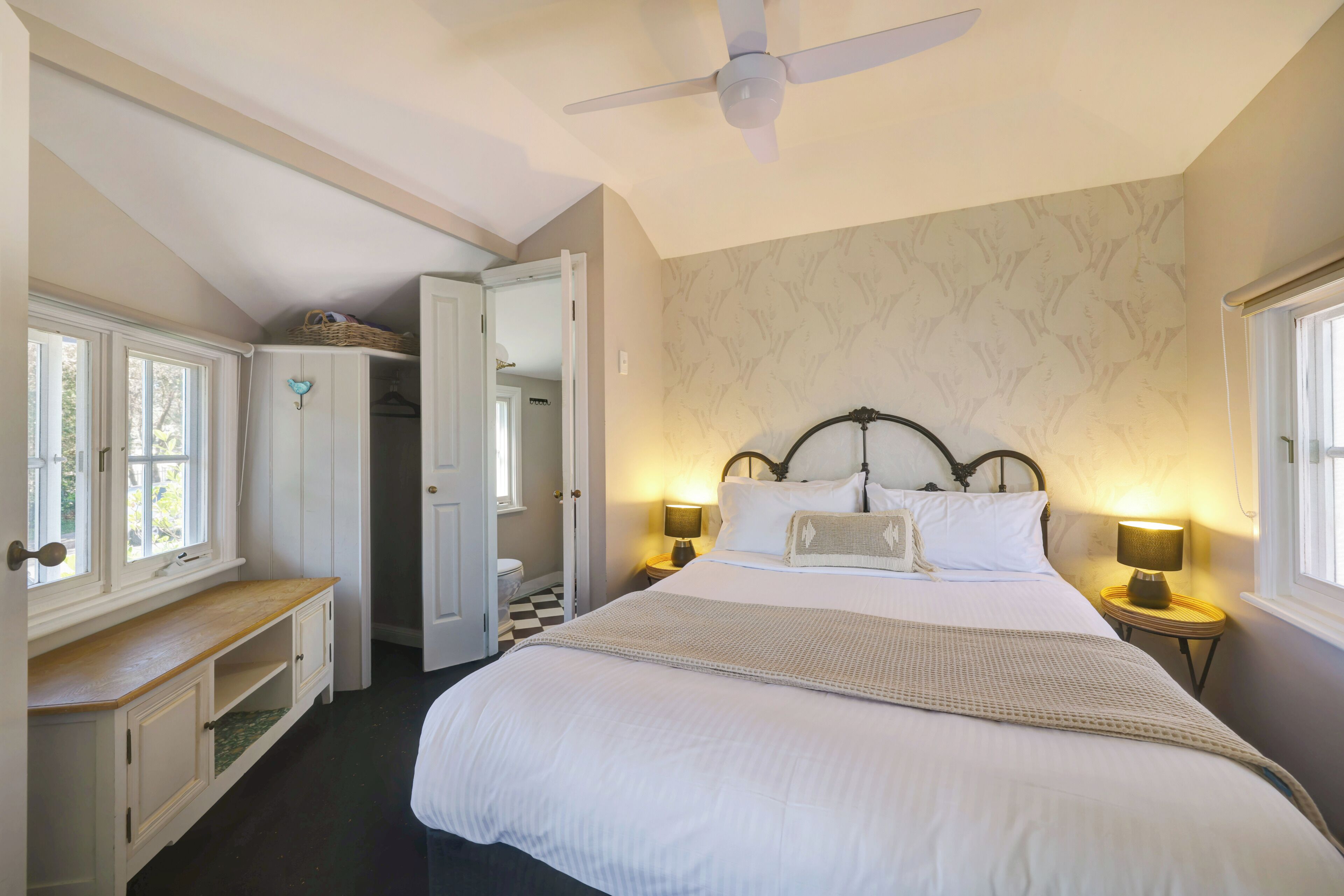 A bedroom with a bed, bedside lamps, a ceiling fan, and a window.