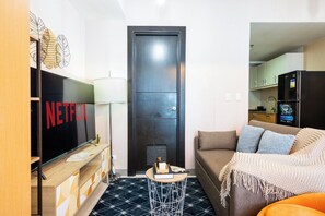 Une chambre d’hôtel moderne équipée d’un téléviseur à écran plat, d’un canapé, d’une petite table ronde et d’une kitchenette.