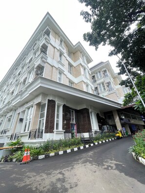 A multi-story building with a prominent entrance, a covered walkway, and a vehicle parked in front. - Apple 1 Condovilla (Jakarta Selatan)