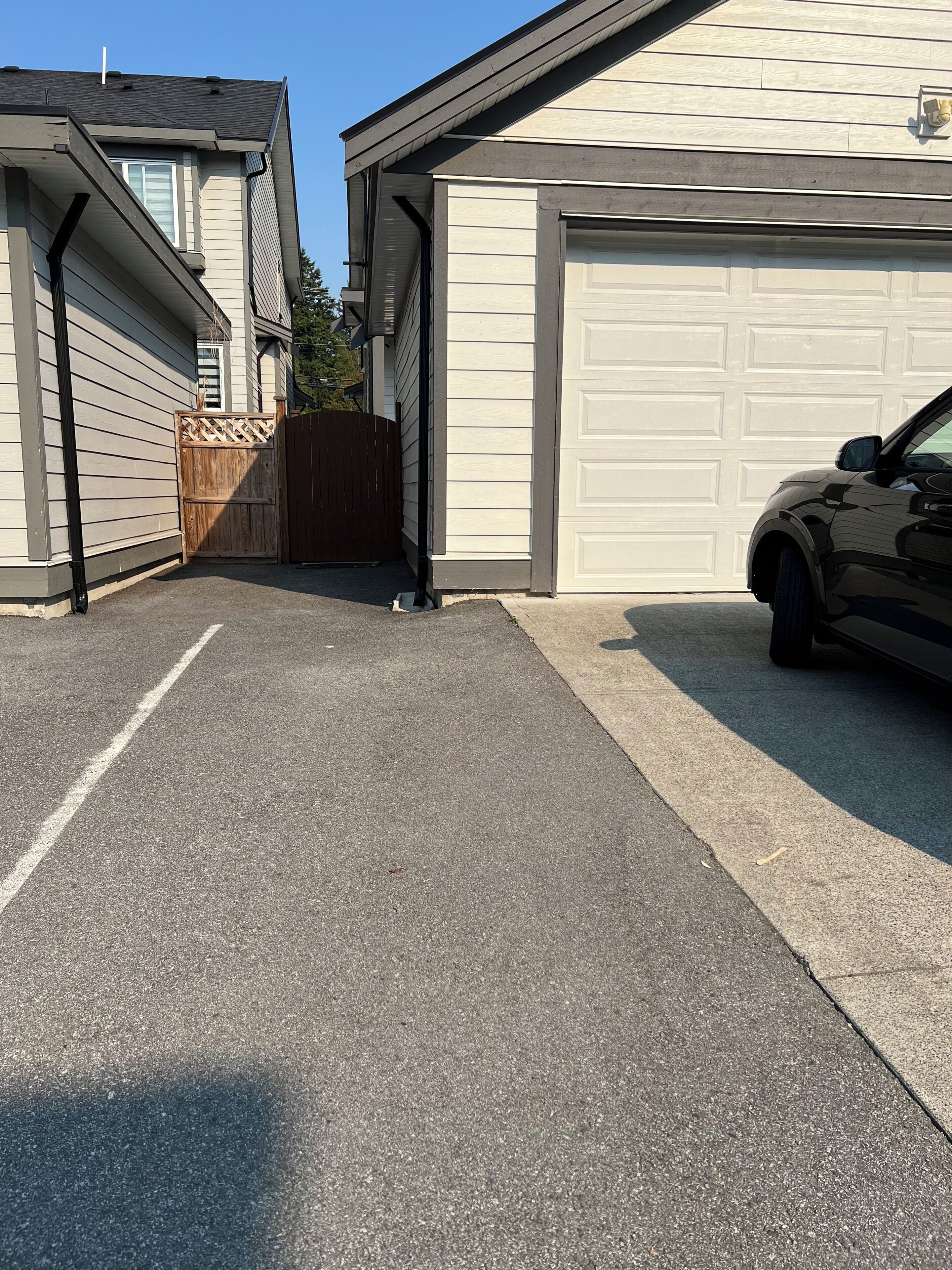 A residential garage with a car parked inside, a wooden gate, and a driveway leading to the garage.