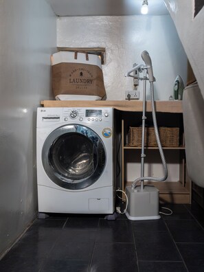 Uma área de lavanderia compacta, equipada com máquina de lavar, secadora e ferro a vapor.