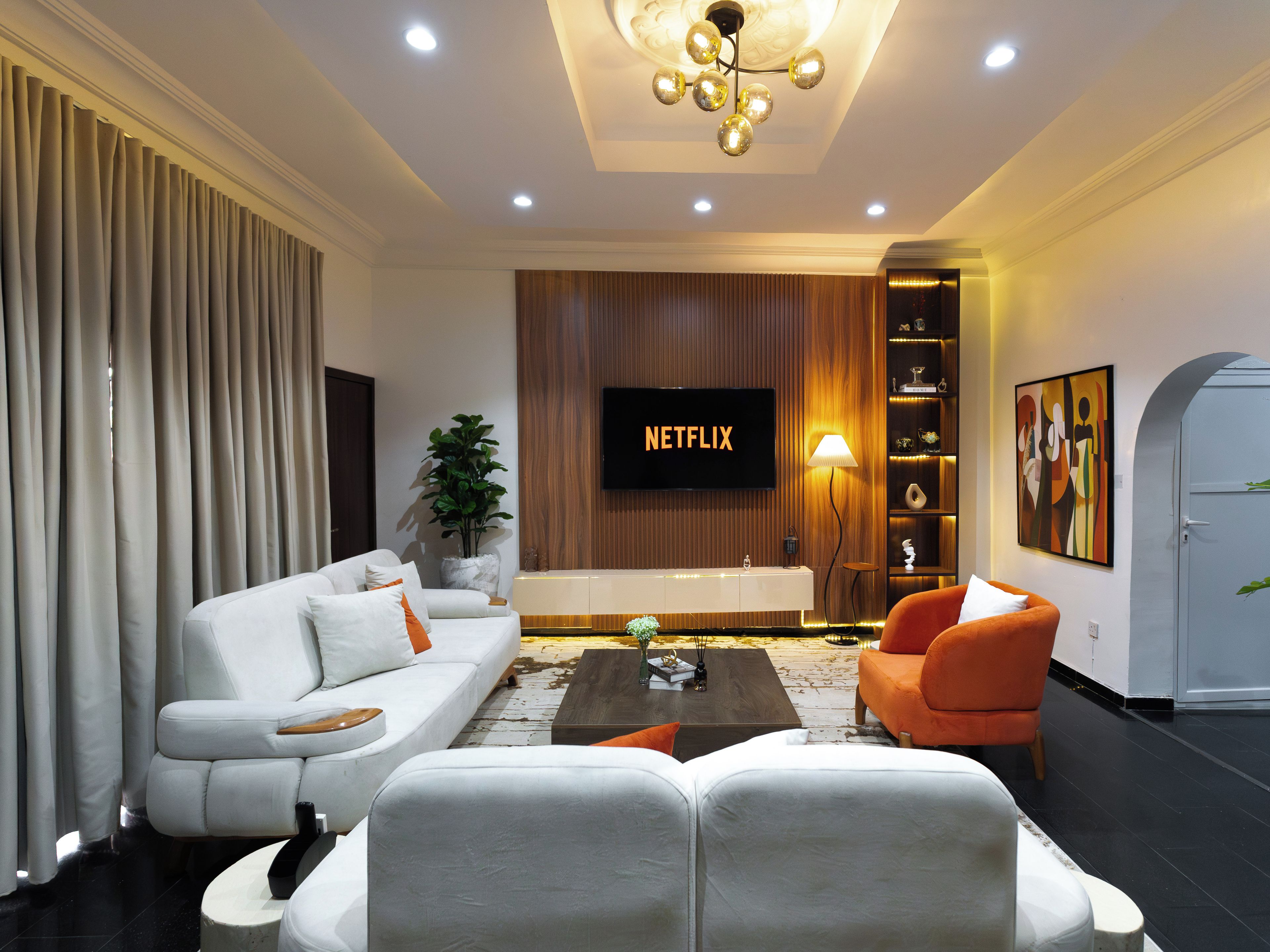 Una sala de estar moderna con un sofá, sillones, una mesa de centro, un televisor y una estantería.