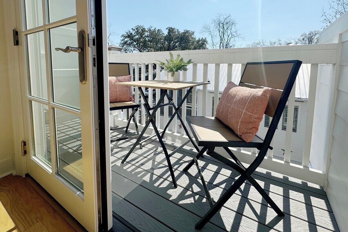 Une terrasse extérieure avec une table et des chaises, une clôture blanche et, au loin, une maison.