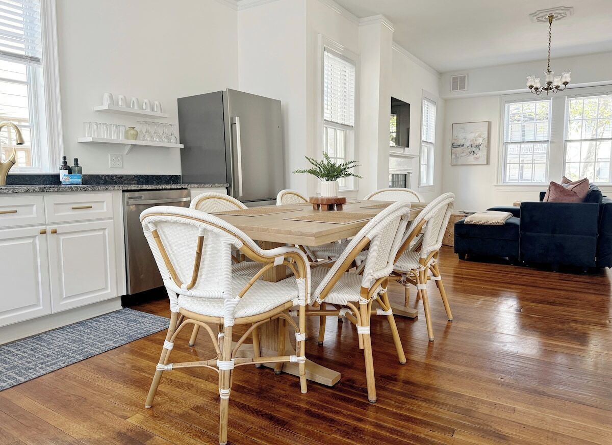 A modern kitchen with white cabinetry, a dining table with wicker chairs, and a dark-colored refrigerator.