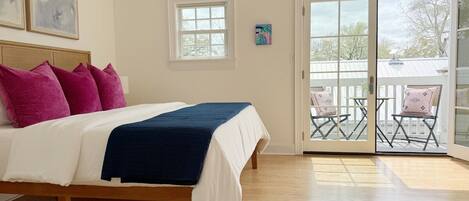 A bedroom with a bed, a balcony with chairs, and a view of the outside.