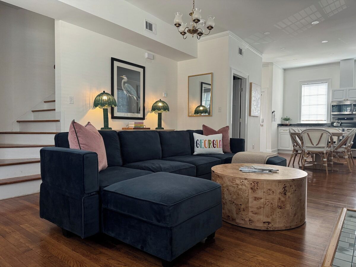Un salon moderne avec un canapé d’angle, un pouf et une table basse ronde.
