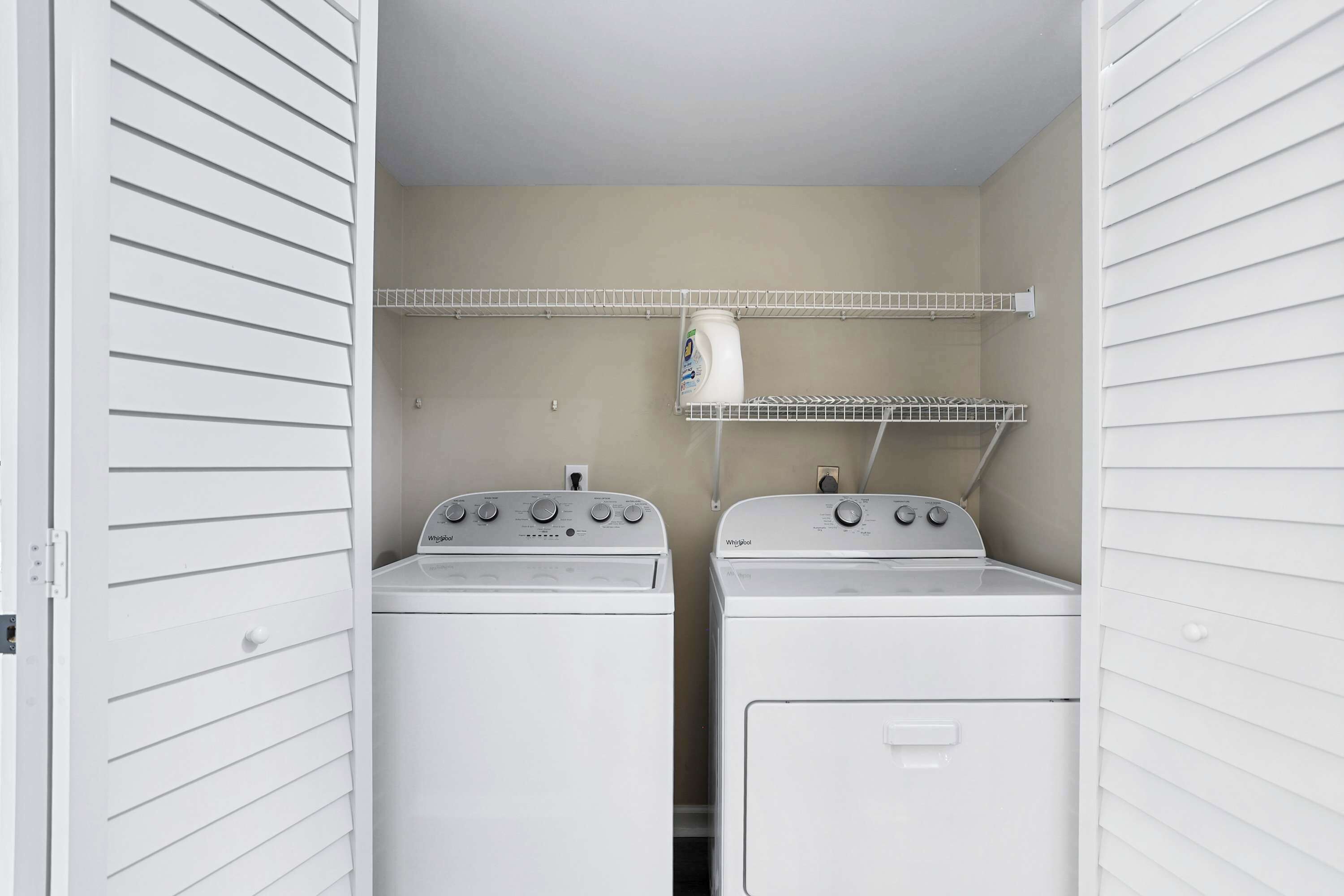 Une buanderie équipée de deux machines à laver et deux sèche-linge superposés, d’une étagère contenant de la lessive et d’une porte dotée d’une poignée.