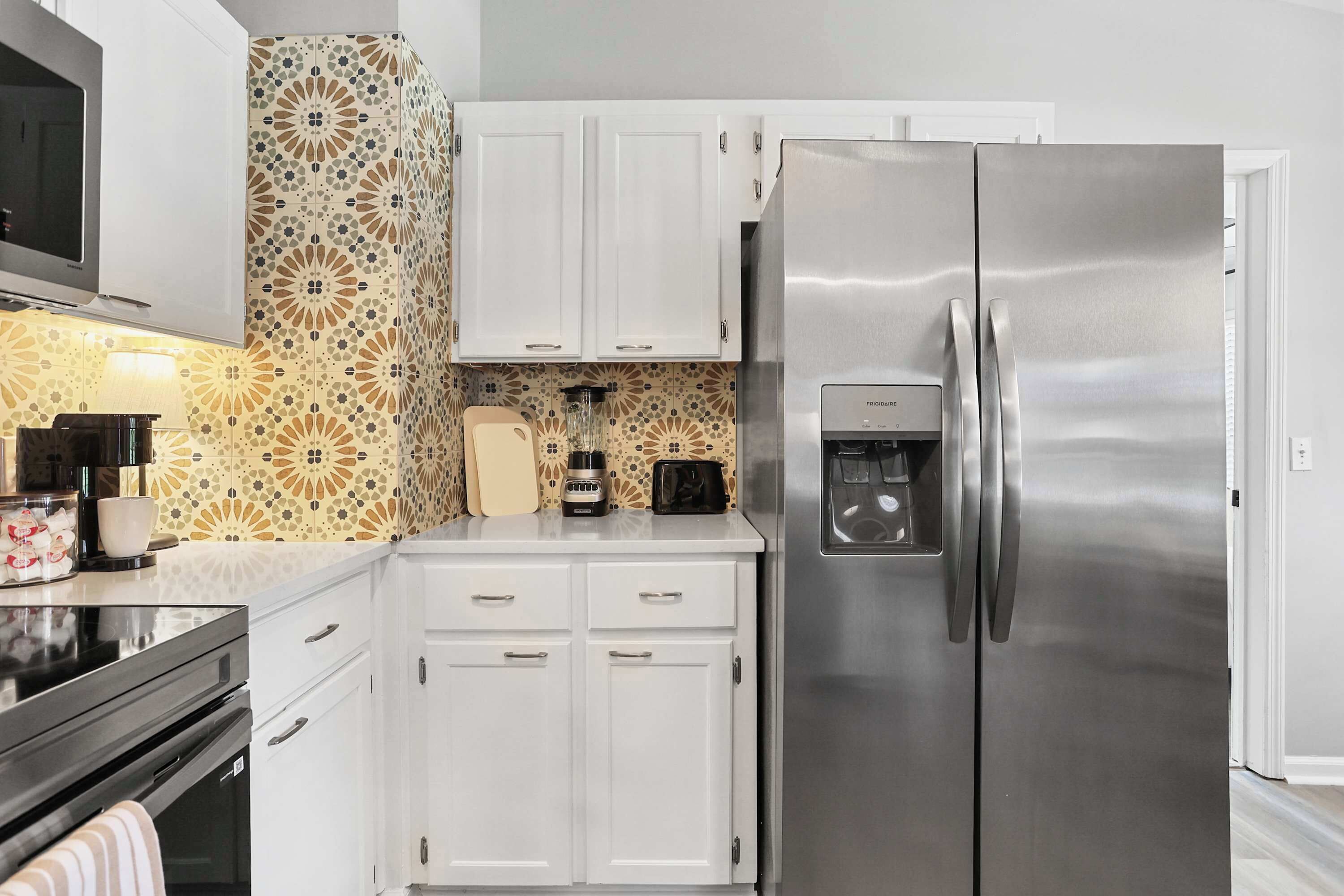 Une cuisine moderne avec des meubles blancs, un réfrigérateur en acier inoxydable et un pare-feu décoratif.