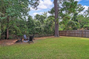 A backyard with a wooden fence, a grassy lawn, and a cluster of Adirondack chairs. - Halfway to Tybee Beach and Downtown Savannah: Renovated Cottage, Dogs Welcome (Savannah)