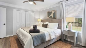 Een slaapkamer met een bed, nachtkastjes, een plafondventilator, een raam met zonwering en een deur.