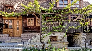 Una casa de madera rústica con cimientos de piedra, un porche de madera y un jardín lleno de flores.